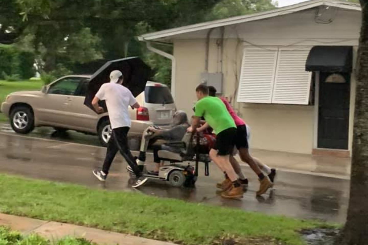 Four young men push elderly woman home after her electric scooter broke down in the pouring rain.